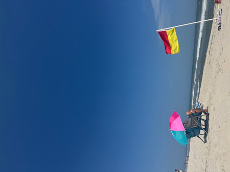 Beach chair with a red and yellow flag and a pink and blue umbrellaの写真素材