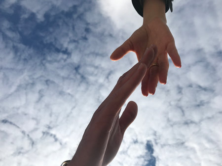 Two hands holding each other against the blue sky with white clouds.