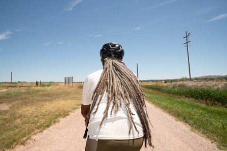 Rear view of a senior woman with dreadlocks biking along a country roadの写真素材