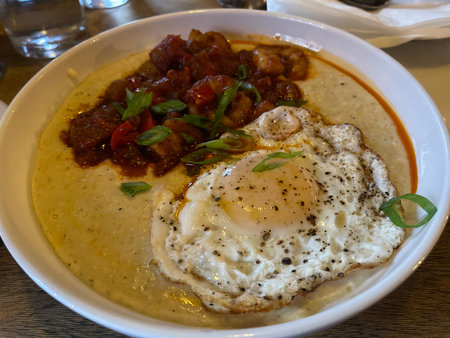 Fried eggs with pork and tomato on a plate in a restaurantの写真素材