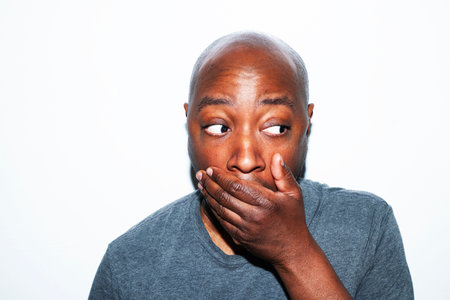 Portrait of a young african american man covering his mouth against white background