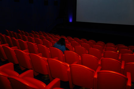 Empty cinema auditorium with rows of red seats and blank screen.の写真素材