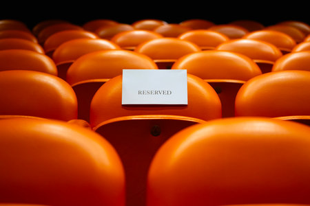 Empty orange seats in a stadium with a white card on it.の写真素材