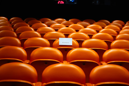 Orange seats in an empty stadium with a sign.