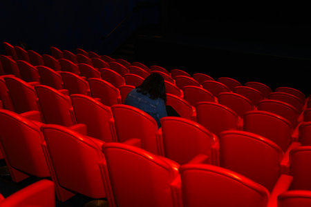 Cinema auditorium with red seats and a woman watching a movieの写真素材