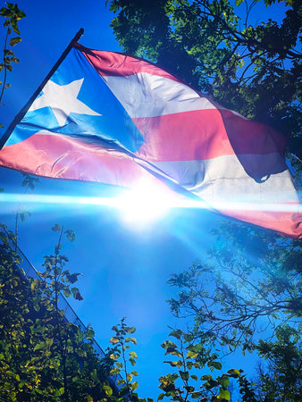 Waving Puerto Rican flag against blue sky with sunbeams.の写真素材