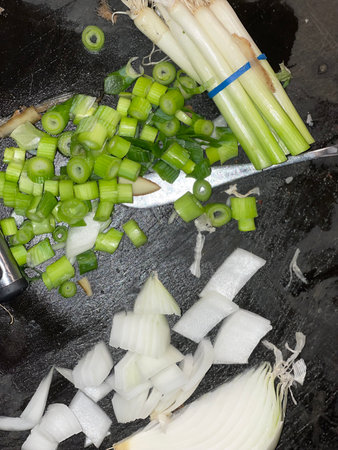 Chopped spring onions and leek on a black kitchen table.の写真素材