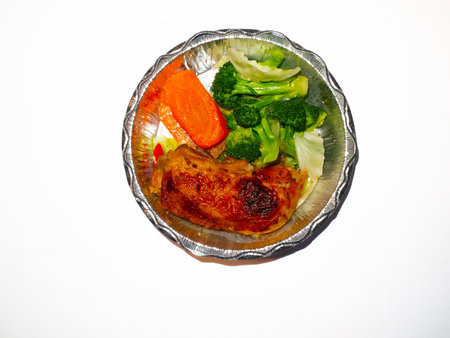 Baked chicken fillet with vegetables in foil tray on white backgroundの写真素材