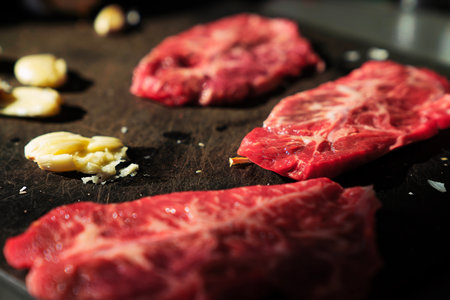 Raw beef steak with garlic on a black cutting board. Selective focus.の写真素材