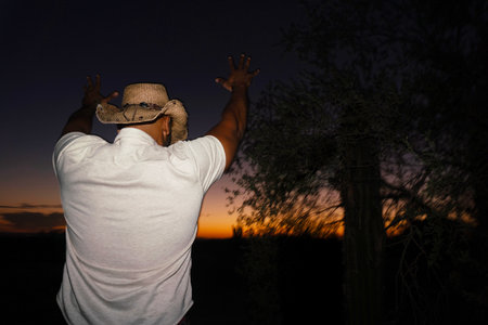 Man in a cowboy hat and white t-shirt on the background of the sunsetの写真素材