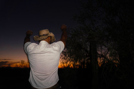Cowboy in cowboy hat with his arms raised looking at the sunsetの写真素材