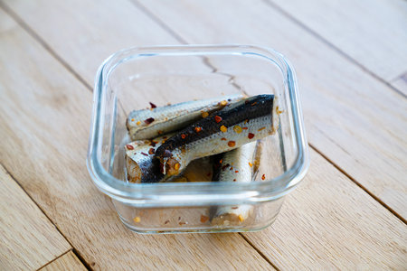 Salted herring in a glass bowl on a wooden background.