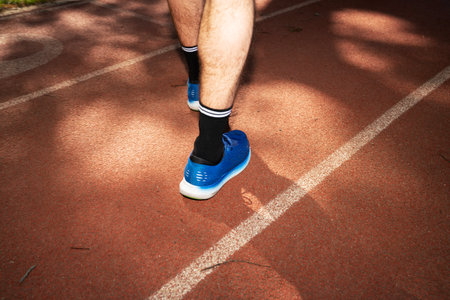 Runner feet on running track. Close-up of athlete legs running on sunny day.