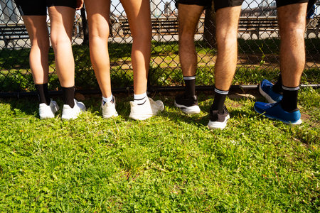 Legs of group of friends standing on green grass in park.