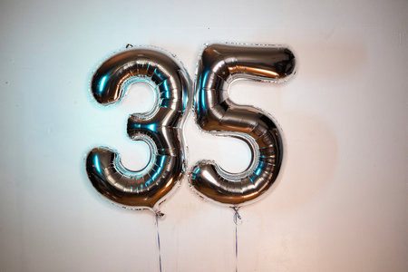 Number 35 gold foil balloon on a white wall. Birthday party decorationの写真素材
