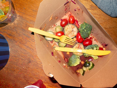 Healthy food in take away box with fork and knife on wooden tableの写真素材