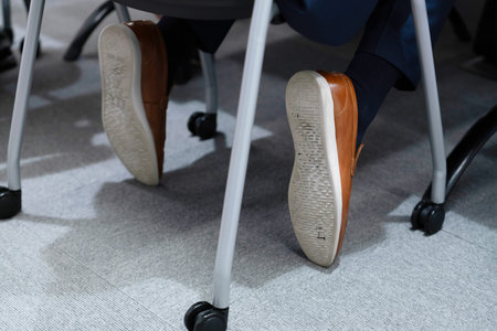 Close-up of business man feet in shoes sitting on office chairの写真素材