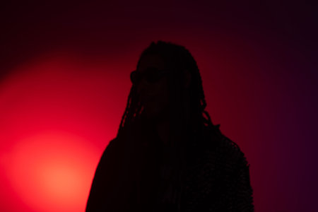 Young woman with dreadlocks posing in front of a red light background