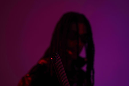 Young woman playing the electric bass guitar on a purple background. Close-up.