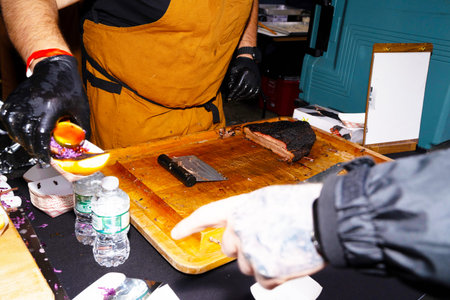 Hands of a person in black gloves and a yellow apron working on a wooden cutting board