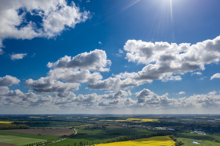 a dreamlike blue sky with white sheep clouds over green and yellow fieldsの写真素材