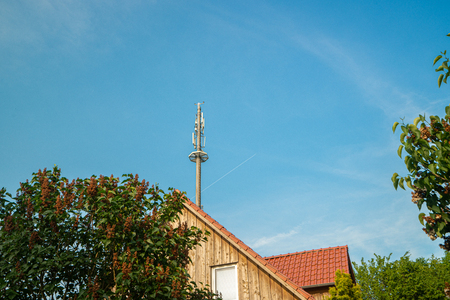 a radio mast for the mobile phone network towers above a residential building into the blue sky in a residential areaの写真素材
