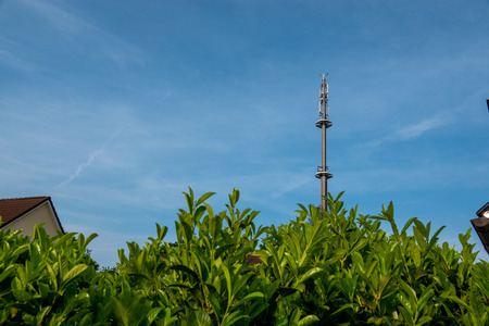 a radio mast for the mobile phone network towers above a residential building into the blue sky in a residential areaの写真素材