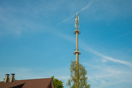 a radio mast for the mobile phone network towers above a residential building into the blue sky in a residential areaの写真素材