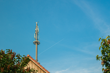 a radio mast for the mobile phone network towers above a residential building into the blue sky in a residential areaの写真素材