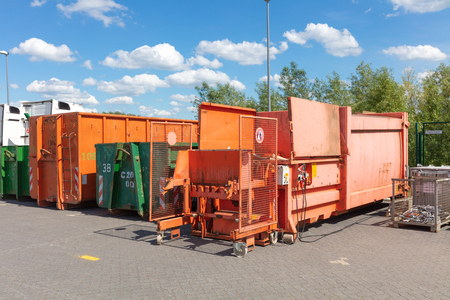 orange waste compactors are standing on a factory site with other waste containers next to themの写真素材