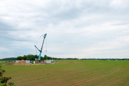 in the middle of a field, a wind turbine is erected with the help of a large craneの写真素材