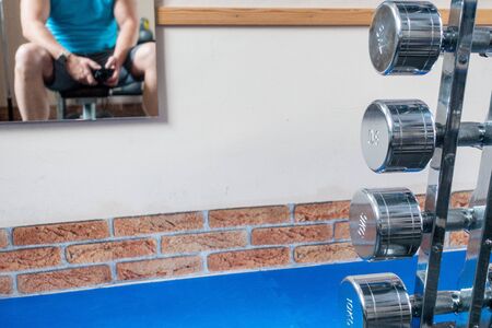 silver dumbbells are in the foreground and a mirror with the mirror image of an athlete hangs on the wallの写真素材