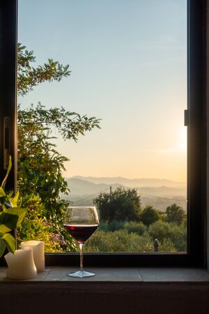 a glass of red wine stands in a window in Tuscanyの写真素材