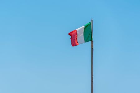 an Italian flag blowing in the wind against a bright blue skyの写真素材