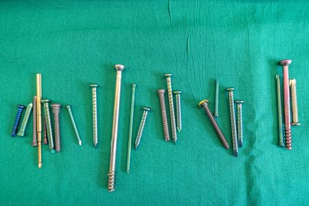 various surgical titanium screws lie spread out on a green surgical drape