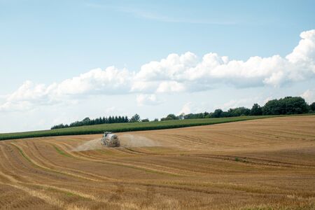 a tractor on which a trailer filled with liquid manure hangs drives over a field and sprays the liquid slurryの写真素材