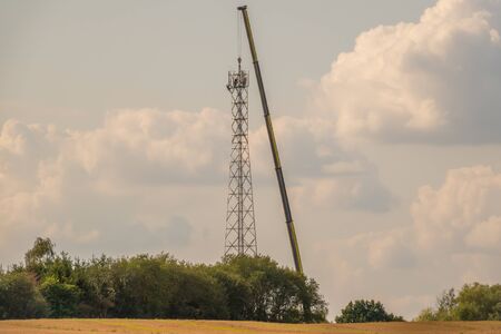 A 5G transmission tower is erected on a field with the help of a huge craneの写真素材
