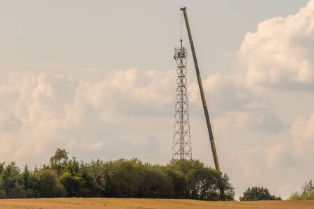 A 5G transmission tower is erected on a field with the help of a huge craneの写真素材