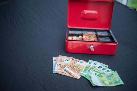 a lot of euro banknotes lie spread out in front of a red cash boxの写真素材