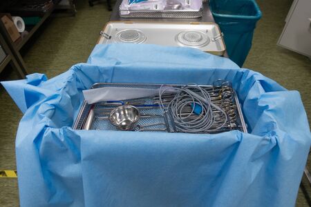 In a sterilization department in a hospital, cleaned instruments are wrapped in a blue cloth before the container is sterilized.の写真素材