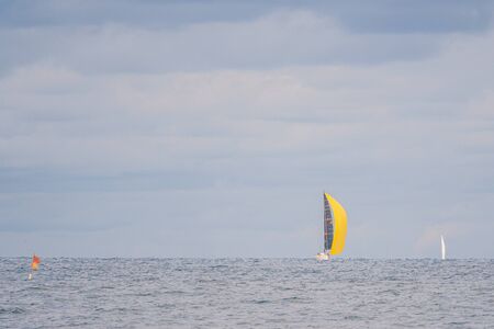 far on the sea floats a sailboat with a bright yellow sail and the sky is full of cloudsの写真素材
