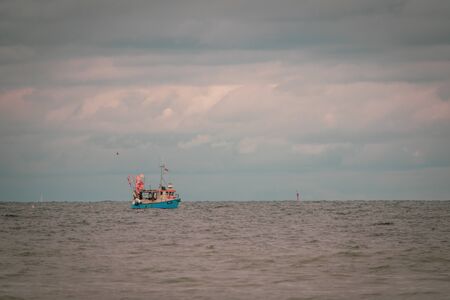 far on the sea floats a fishing boat, which is surrounded by many seagulls and the sky is full of cloudsの写真素材