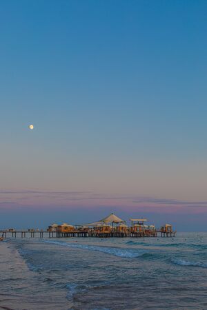 Im Vordergrund steht ein Badesteg im Meer und im Hintergrund steht der Mond am Himmel wÃ¤hrend des Sonnenuntergangesの写真素材