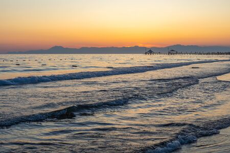 on a beach in the foreground are the waves and in the background is a golden sunsetの写真素材