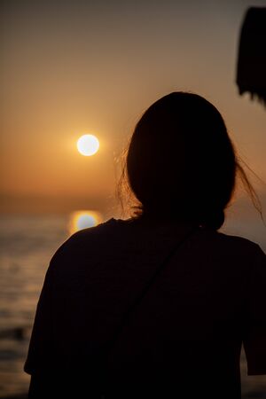 the silhouette of a young woman stands in the Voerdergrund and in the background is a golden sunsetの写真素材