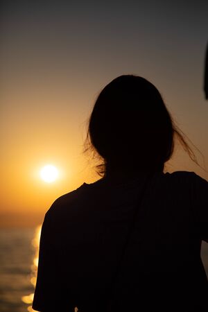 the silhouette of a young woman stands in the Voerdergrund and in the background is a golden sunsetの写真素材
