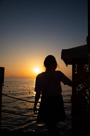 the silhouette of a young woman stands in the Voerdergrund and in the background is a golden sunsetの写真素材