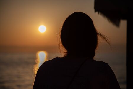 the silhouette of a young woman stands in the Voerdergrund and in the background is a golden sunsetの写真素材
