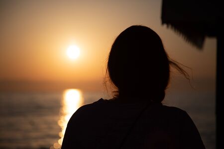 the silhouette of a young woman stands in the Voerdergrund and in the background is a golden sunsetの写真素材