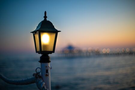 a lantern on a bathing jetty glows bright yellow at duskの写真素材